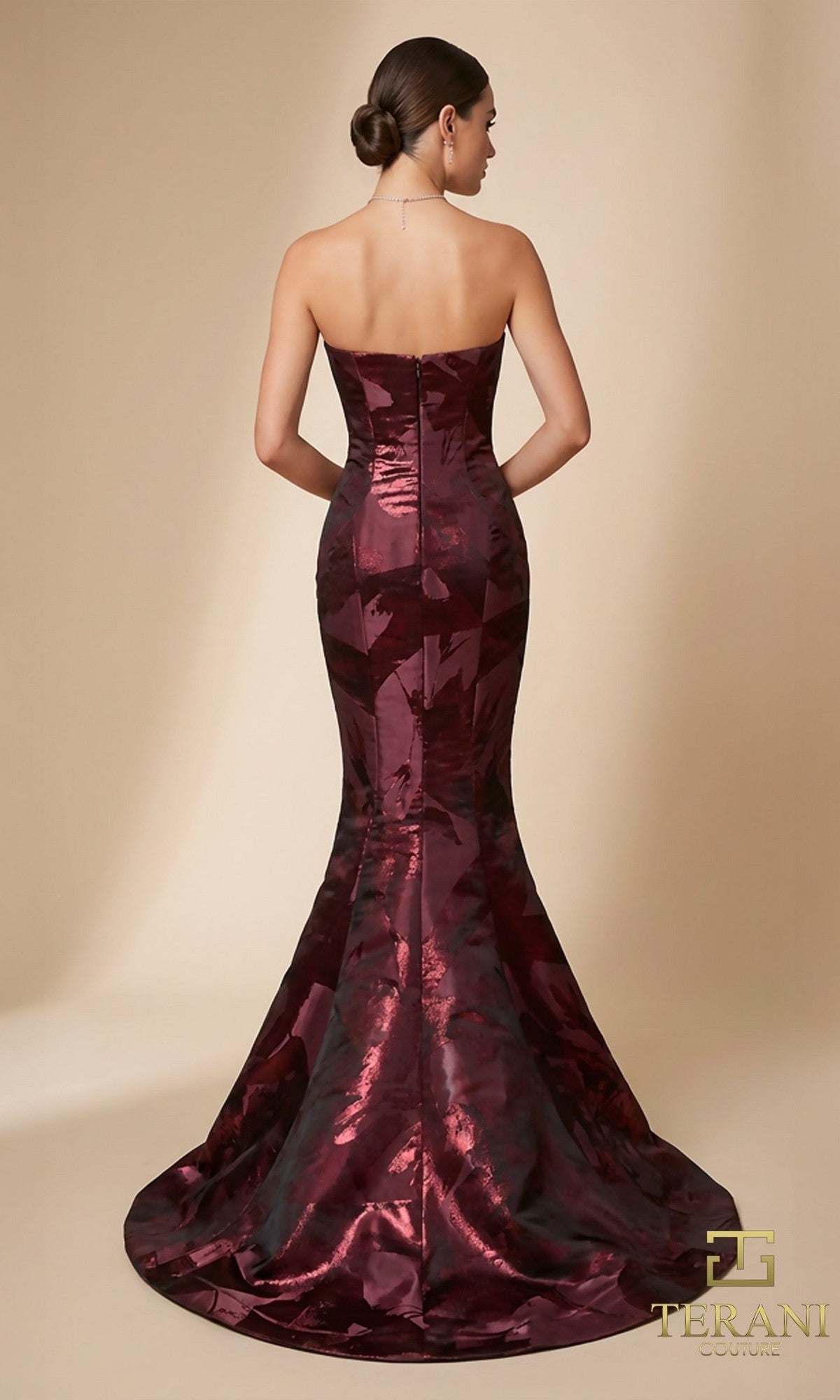 Woman in a strapless burgundy mermaid gown with a slight train, posing with her back to the camera against a neutral background. She wears the elegant Long Formal Dress: Terani 261E6259.